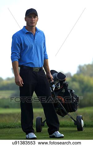Stock Image - Portrait of young man carrying trolley with golf bag. Fotosearch
