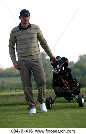 Stock Photograph - Portrait of young man carrying trolley with golf bag. Fotosearch