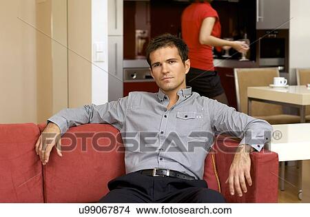 Portrait of young man relaxing in sofa, woman in background View Large Photo Image Picture - Portrait of young man relaxing in sofa, woman in background. Fotosearch