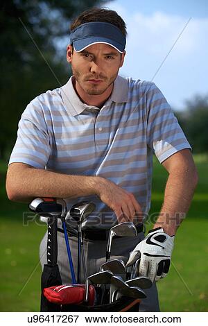Stock Photo - Portrait of young man standing by golf bag full of sticks. Fotosearch