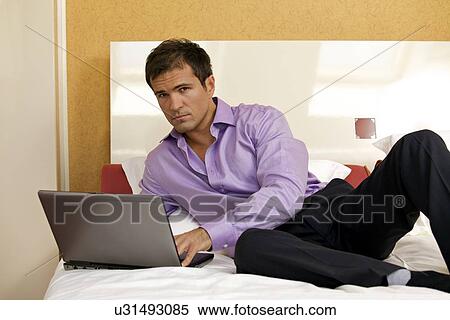 Portrait of young man using laptop on bed View Large Photo Image Stock Photography - Portrait of young man using laptop on bed. Fotosearch
