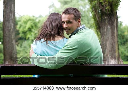 Stock Image - Portrait of young man with girlfriend sitting on bench. Fotosearch