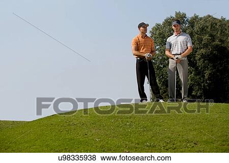 Portrait of young men standing with golf sticks on golf course View Large Photo Image Stock Photo - Portrait of young men standing with golf sticks on golf course. Fotosearch