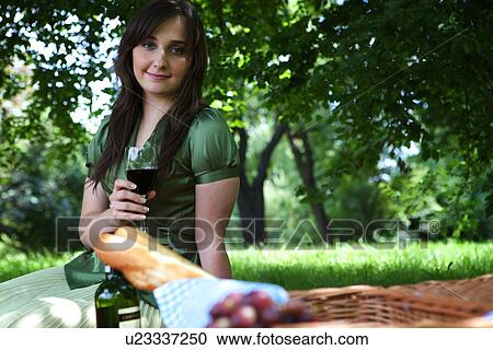 Portrait of young woman holding wineglass, sitting in park View Large Photo Image Stock Image - Portrait of young woman holding wineglass, sitting in park. Fotosearch