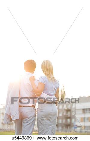 Rear view of business couple standing with arms around against clear sky on sunny day View Large Photo Image Stock Image - Rear view of business couple standing with arms around against clear sky on sunny day. Fotosearch