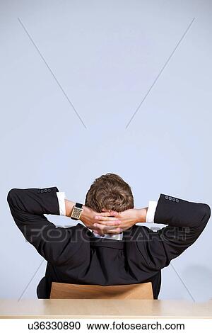 Rear view of businessman sitting in office with hands behind head View Large Photo Image Stock Image - Rear view of businessman sitting in office with hands behind head. Fotosearch