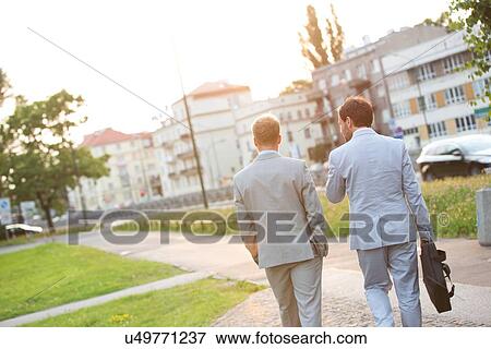 Stock Photo - Rear view of businessmen walking at park on sunny day. Fotosearch