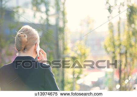 Stock Photography - Rear view of businesswoman using cell phone on sunny day. Fotosearch