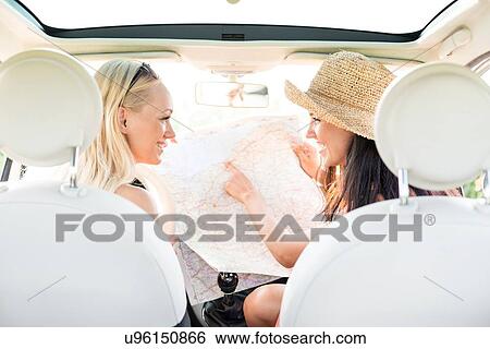 Rear view of happy female friends reading map in car View Large Photo Image Stock Photograph - Rear view of happy female friends reading map in car. Fotosearch