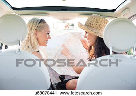 Stock Image - Rear view of happy women reading map in car. Fotosearch