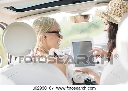 Rear view of happy women using digital tablet in car View Large Photo Image Stock Photo - Rear view of happy women using digital tablet in car. Fotosearch