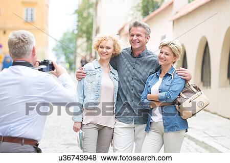 Stock Photo - Rear view of man photographing friends in city. Fotosearch