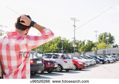 Stock Photograph - Rear view of man with hand behind head standing on city street against clear sky. Fotosearch