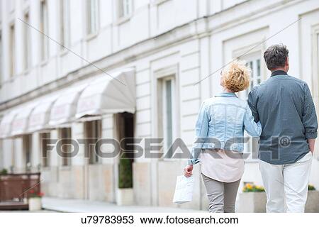 Rear view of middle-aged couple walking by building View Large Photo Image Stock Image - Rear view of middle-aged couple walking by building. Fotosearch
