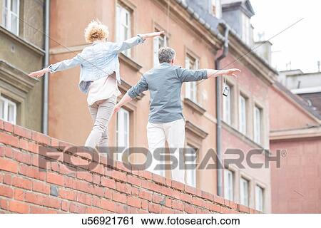 Rear view of middle-aged couple with arms outstretched walking on brick wall View Large Photo Image Stock Image - Rear view of middle-aged couple with arms outstretched walking on brick wall. Fotosearch