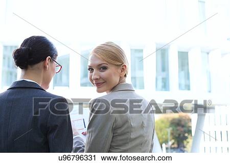 Stock Image - Rear view of portrait of smiling businesswoman sitting with colleague outdoors. Fotosearch