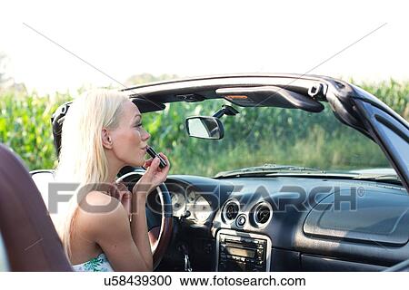 Rear view of woman applying lipstick in convertible View Large Photo Image Stock Image - Rear view of woman applying lipstick in convertible. Fotosearch