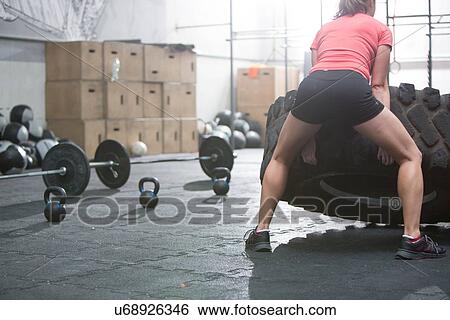 Rear view of woman flipping tire in crossfit gym View Large Photo Image Stock Photograph - Rear view of woman flipping tire in crossfit gym. Fotosearch