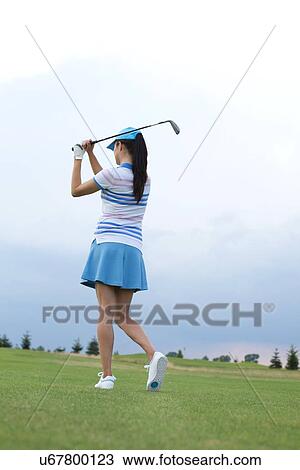 Rear view of woman swinging golf club at course View Large Photo Image Stock Image - Rear view of woman swinging golf club at course. Fotosearch