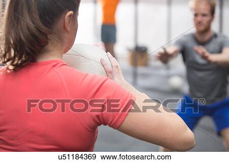 Rear view of woman throwing medicine ball towards man in crossfit gym View Large Photo Image Stock Photo - Rear view of woman throwing medicine ball towards man in crossfit gym. Fotosearch