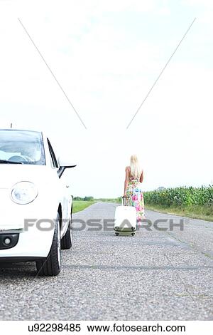 Rear view of woman with luggage leaving broken down car on country road View Large Photo Image Stock Photography - Rear view of woman with luggage leaving broken down car on country road. Fotosearch