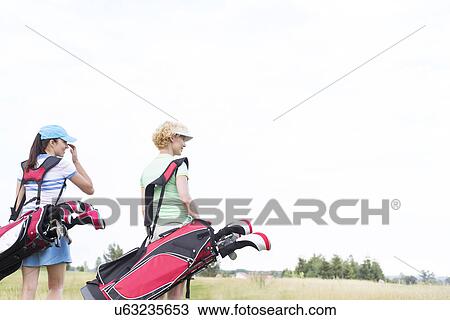 Rear view of women with golf club bags at course against clear sky View Large Photo Image Stock Image - Rear view of women with golf club bags at course against clear sky. Fotosearch
