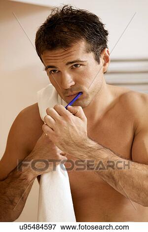 Stock Photo - Reflection in a bathroom mirror of a young man brushing his teeth. Fotosearch