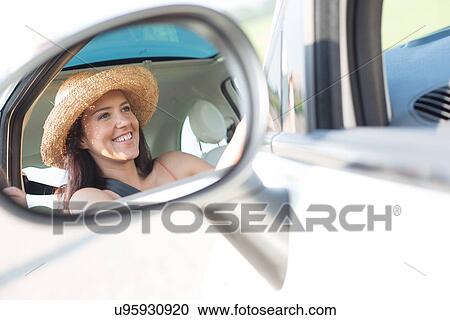 Stock Image - Reflection of happy woman in rearview mirror of car. Fotosearch