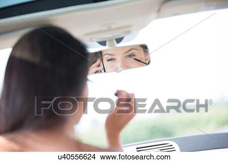 Reflection of woman using cell phone while applying mascara in rearview mirror of car View Large Photo Image Picture - Reflection of woman using cell phone while applying mascara in rearview mirror of car. Fotosearch