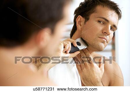 Reflection of young man in mirror shaving with electric shaver View Large Photo Image Stock Image - Reflection of young man in mirror shaving with electric shaver. Fotosearch