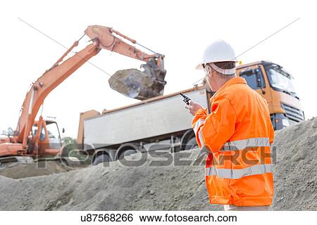 Side view of architect using walkie-talkie while working at construction site View Large Photo Image Stock Photograph - Side view of architect using walkie-talkie while working at construction site. Fotosearch