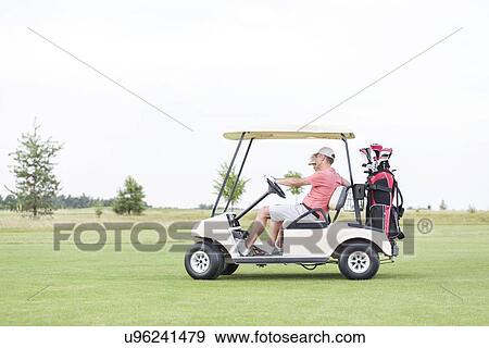 Stock Photo - Side view of couple sitting in golf cart against clear sky. Fotosearch