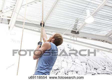 Side view of dedicated man climbing rope in crossfit gym View Large Photo Image Picture - Side view of dedicated man climbing rope in crossfit gym. Fotosearch