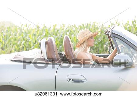Stock Image - Side view of woman driving convertible on sunny day. Fotosearch