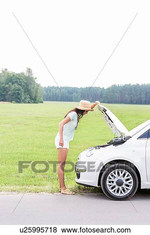 Side view of woman examining broken down car on country road View Large Photo Image Stock Photo - Side view of woman examining broken down car on country road. Fotosearch