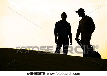 Silhouette of young men standing in golf course with trolley View Large Photo Image Stock Photo - Silhouette of young men standing in golf course with trolley. Fotosearch