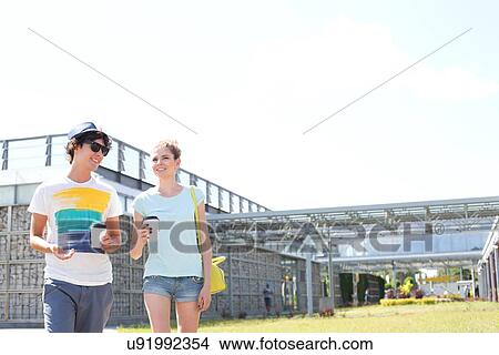 Picture - Smiling couple holding disposable cups while walking at park. Fotosearch