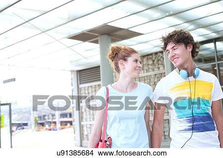 Smiling couple looking at each other while walking in city View Large Photo Image Picture - Smiling couple looking at each other while walking in city. Fotosearch