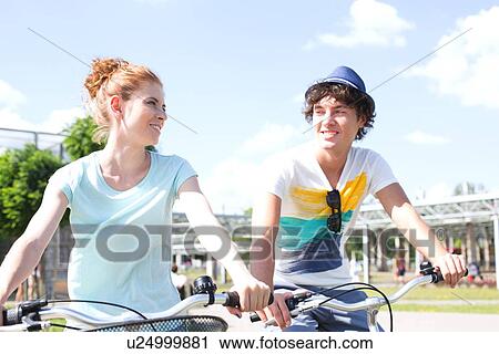Stock Image - Smiling couple looking at each other while cycling in city. Fotosearch