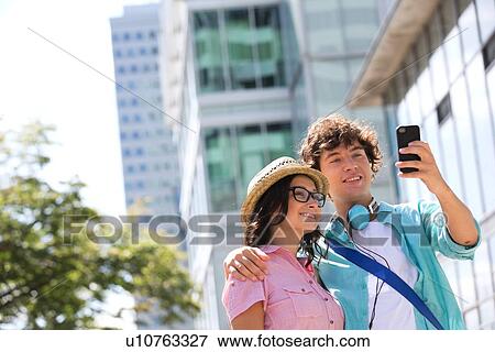 Smiling couple taking self portrait outside office building View Large Photo Image Stock Photo - Smiling couple taking self portrait outside office building. Fotosearch