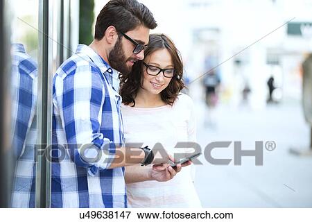 Smiling couple using smart phone together in city View Large Photo Image Stock Photo - Smiling couple using smart phone together in city. Fotosearch