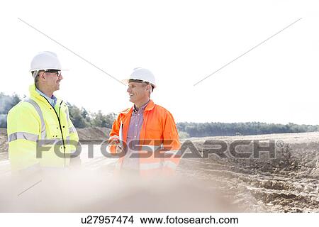 Smiling engineers discussing at construction site on sunny day View Large Photo Image Picture - Smiling engineers discussing at construction site on sunny day. Fotosearch