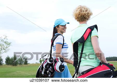 Stock Photo - Smiling female golfer talking to friend at golf course. Fotosearch
