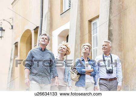 Stock Image - Smiling friends looking up while walking by building. Fotosearch
