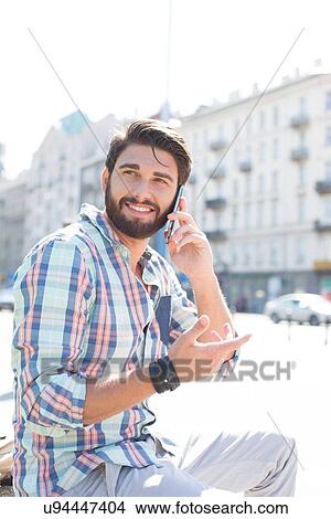 Picture - Smiling man looking away while using cell phone in city. Fotosearch