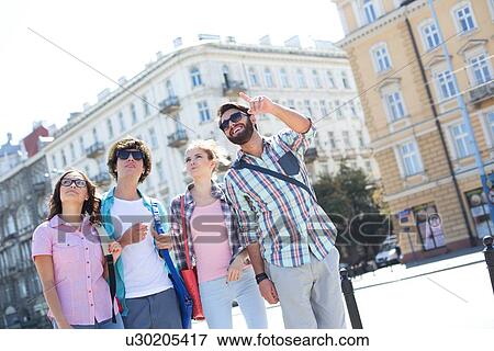 Smiling man showing something to friends on city street View Large Photo Image Stock Photo - Smiling man showing something to friends on city street. Fotosearch