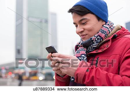 Smiling man using cell phone in city during winter View Large Photo Image Picture - Smiling man using cell phone in city during winter. Fotosearch