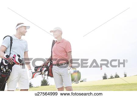 Stock Photo - Smiling men talking at golf course against clear sky. Fotosearch