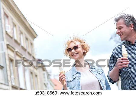 Smiling middle-aged couple holding ice cream cones on sunny day View Large Photo Image Stock Photo - Smiling middle-aged couple holding ice cream cones on sunny day. Fotosearch