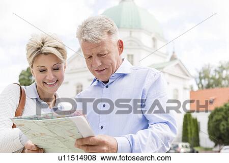 Stock Photo - Smiling middle-aged couple reading map outdoors. Fotosearch